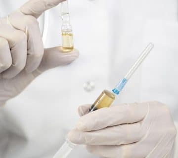 Front view doctor with surgical gloves holding medication syringe 360x320